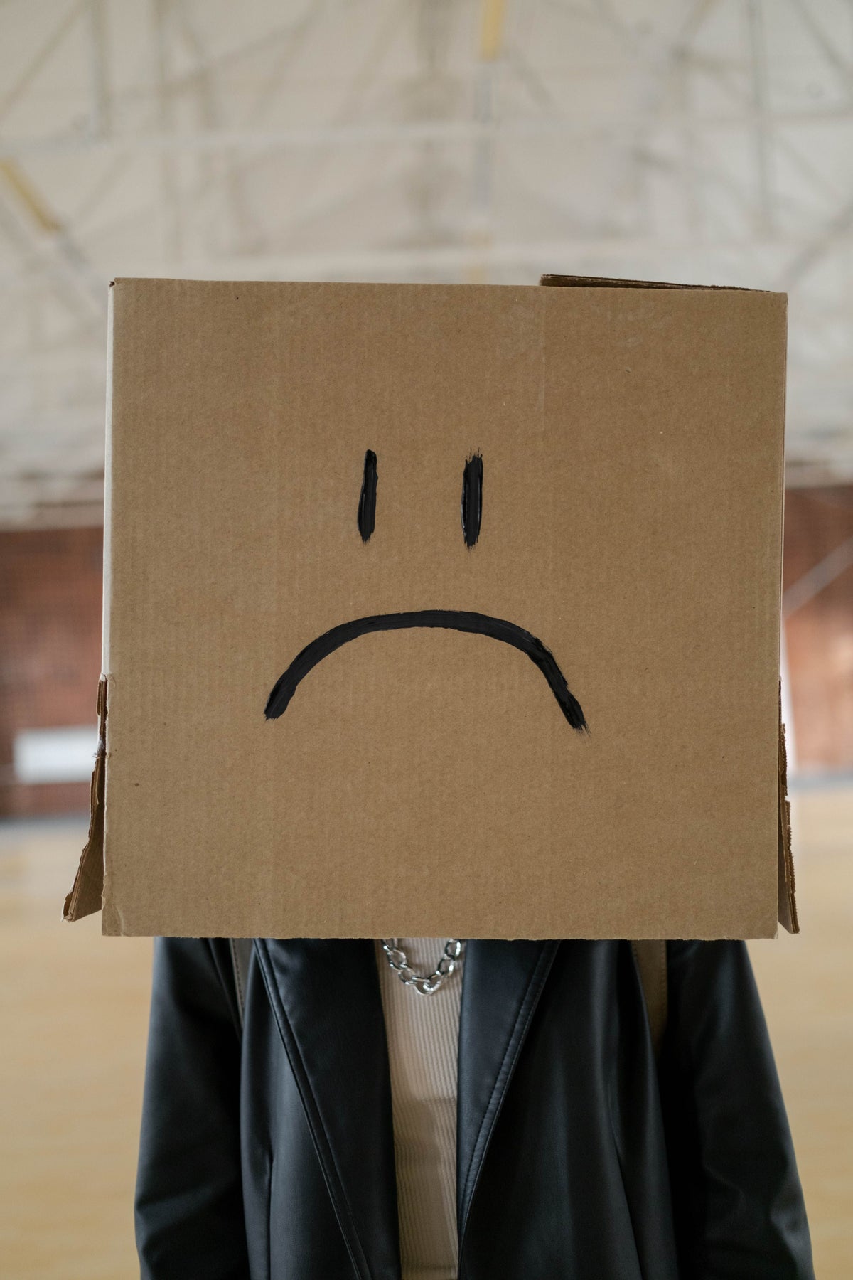 Person wearing a cardboard box with a frowning face drawn on it